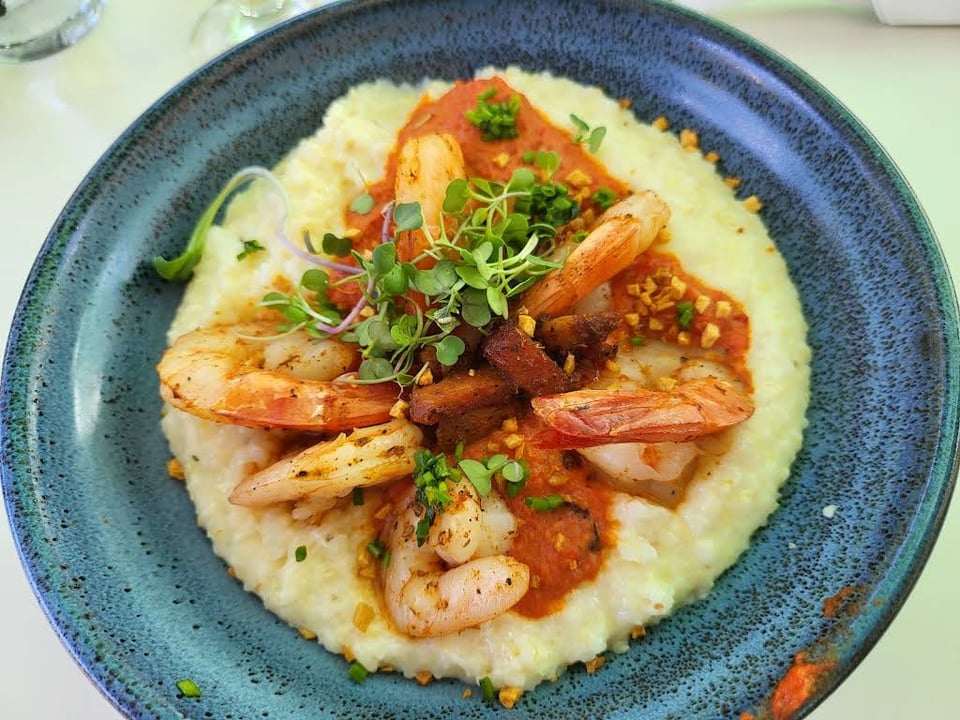 Shrimp and grits with red sauce and greens on a blue plate at Collins Quarter at Forsyth.