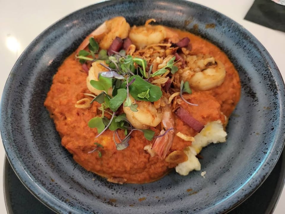 Shrimp over orange grits with herbs on a blue plate at Collins Quarter at Forsyth.