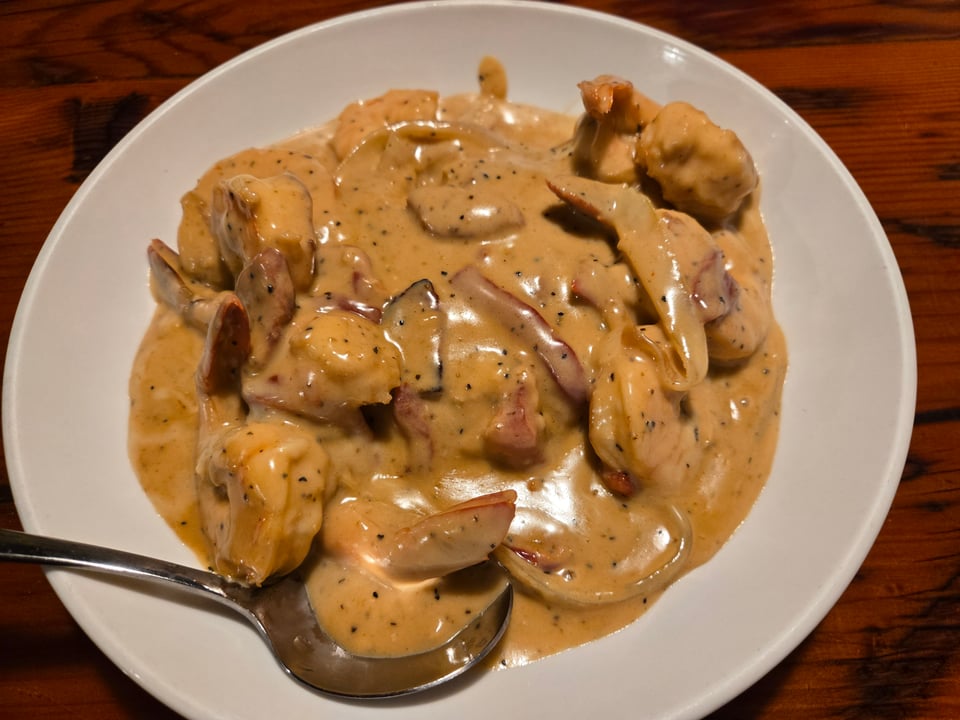 Overhead view of a white plate with shrimp and grits covered in creamy orange sauce, with a serving spoon at the edge.