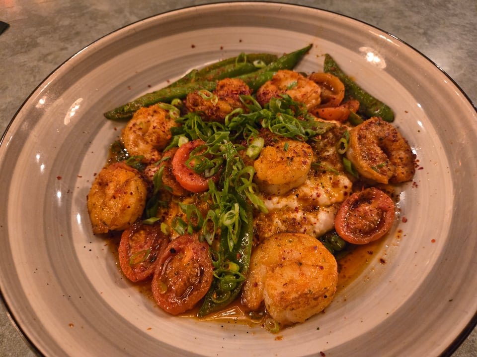 Close view of shrimp over grits with snap peas, tomatoes, sliced scallions, and seasoned butter sauce at Repeal 33.