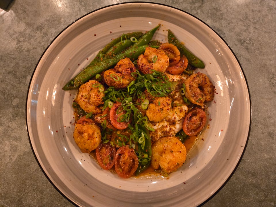 Overhead view of seven shrimp arranged with tomatoes and snap peas over grits in a wide-rimmed plate at Repeal 33.