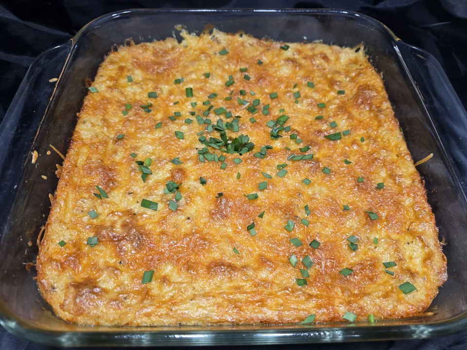 A square glass baking dish of baked cheesy grits with a golden, browned cheese top and chopped chives scattered over it