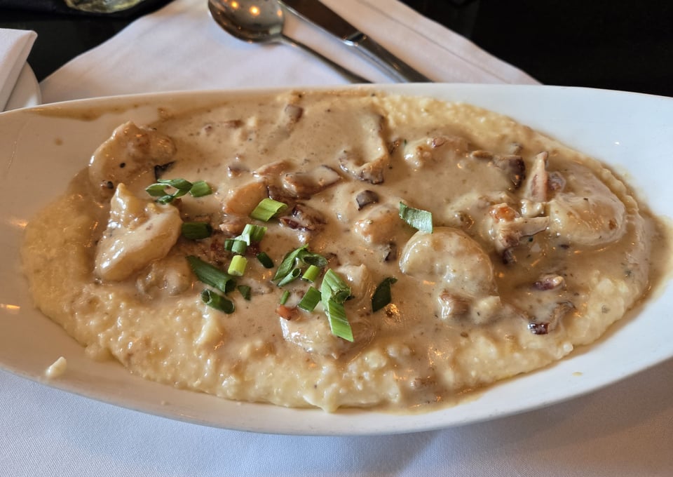 Shrimp and grits topped with rosemary barbecue sauce, bacon, and sliced green onions on a white oval plate.